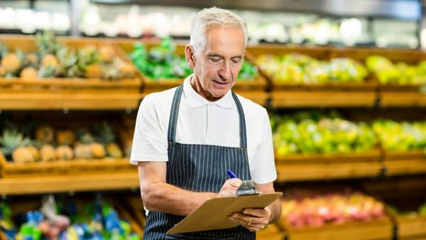 Older grey haired man working in the fruit and vegetable department of a shop